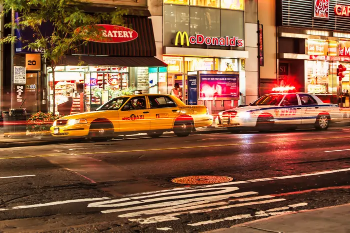 A taxi cab is stopped by a patrol car of the NYPD at night\.